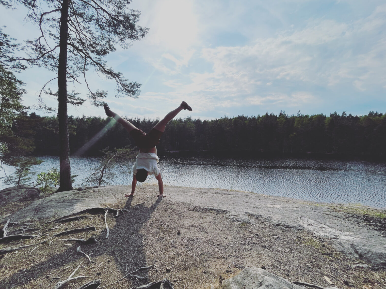 A man doing handstand on the edge of a lake.